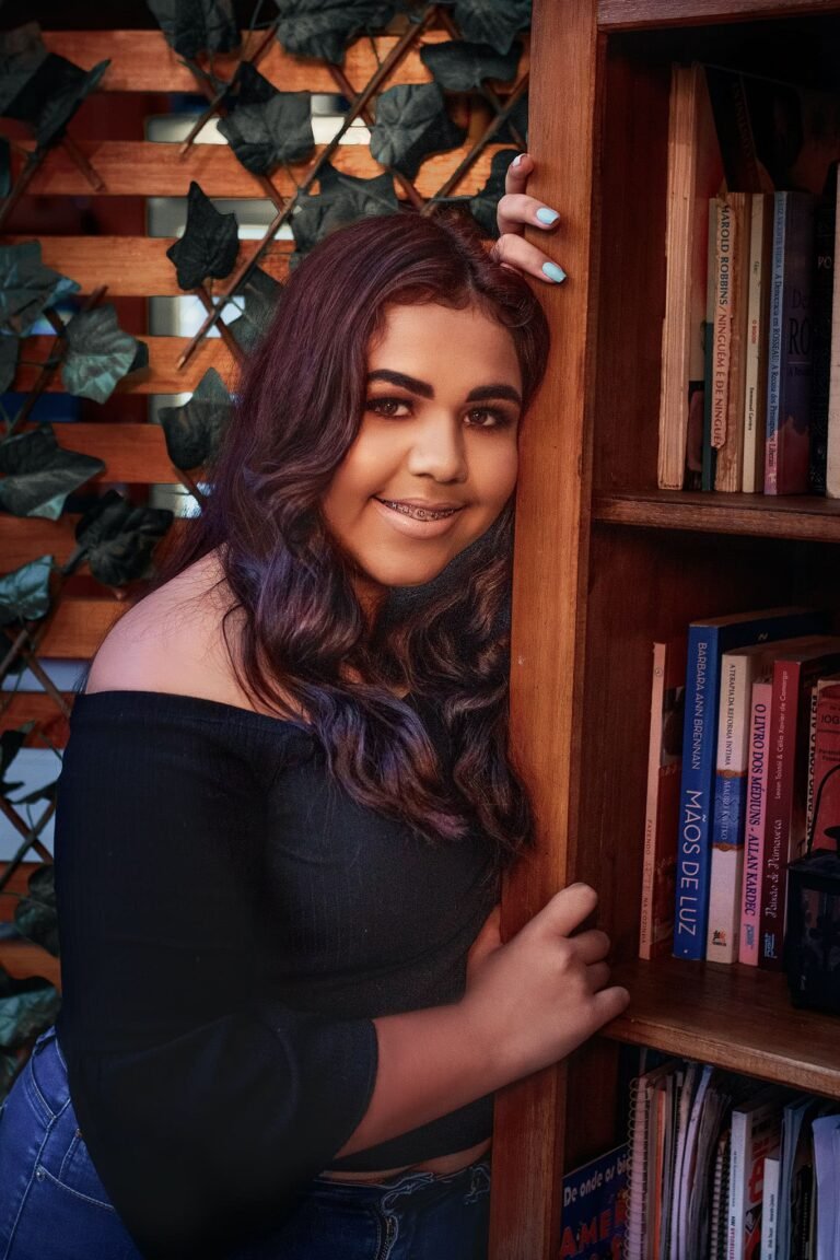 Ensaio fotográfico de 15 anos de Alana em Guaíba, junto à estante de livros, capturando seu sorriso e expressão autêntica
